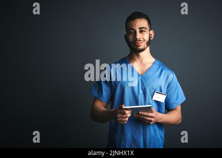 I do my diagnosing in digital format. Studio shot of a young doctor using a digital tablet against a gray background. Stock Photo