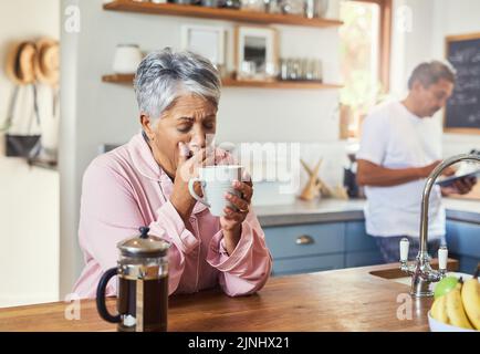 The retired life. a carefree elderly woman sitting at a table in the kitchen drinking coffee and about to sneeze. Stock Photo