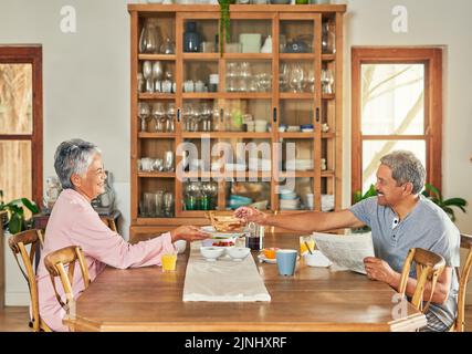 Another slice of toast dear. a cheerful elderly couple having breakfast together around a table at home during the day. Stock Photo