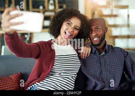 Find the one you can be yourself with. a happy young couple taking selfies together at home. Stock Photo