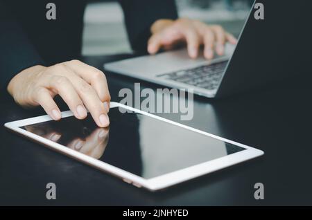 Businessman with a touch tablet and a laptop computer searches for information with Internet technology working at desk. Stock Photo