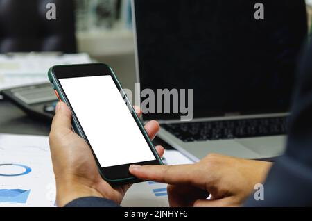 Man holding mobile smartphone mock up blank white screen and computer laptop document graph on desk.clipping pahts. Stock Photo