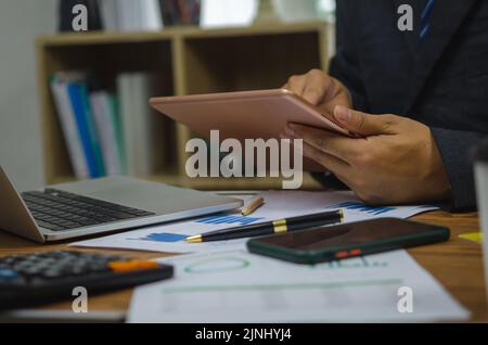 Person businessman holding tablet digital communication technology analysis graph and chart finance on desk. Stock Photo