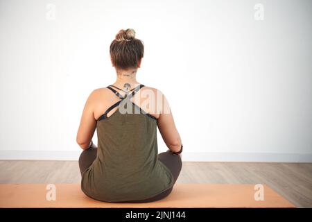 Back view of unrecognizable young woman sitting in lotus position while practicing yoga at spacious health club Stock Photo