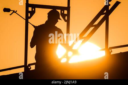 Hanover, Germany. 12th Aug, 2022. A construction worker stands with a gas burner during the construction of an apartment building in the Kronsrode development area as the sun rises on the horizon. The persistent heat is an enormous burden for many workers. Credit: Julian Stratenschulte/dpa/Alamy Live News Stock Photo