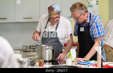 PRODUCTION - 30 June 2022, Lower Saxony, Lüneburg: Winfried Marx, professional chef (l), gives Jörg cooking tips at the cooking group for grieving widowers. The members of the small group, which meets once a month in Lüneburg to cook, are between 59 and 87 years old. A professional guides the widowers. (to dpa-KORR 'Cooking group for grieving widowers - ready meals are taboo') Photo: Philipp Schulze/dpa Stock Photo