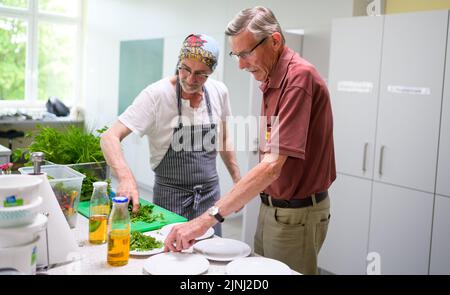 PRODUCTION - 30 June 2022, Lower Saxony, Lüneburg: Winfried Marx, professional chef (l), gives Rainer cooking tips at the cooking group for grieving widowers. The members of the small group, which meets once a month in Lüneburg to cook, are between 59 and 87 years old. A professional guides the widowers. (to dpa-KORR 'Cooking group for grieving widowers - ready meals are taboo') Photo: Philipp Schulze/dpa Stock Photo
