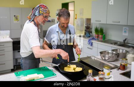 PRODUCTION - 30 June 2022, Lower Saxony, Lüneburg: Winfried Marx, professional chef (l), gives Sven tips on frying at the cooking group for grieving widowers. The members of the small group, which meets once a month in Lüneburg to cook, are between 59 and 87 years old. A professional guides the widowers. (to dpa-KORR 'Cooking group for grieving widowers - ready meals are taboo') Photo: Philipp Schulze/dpa Stock Photo