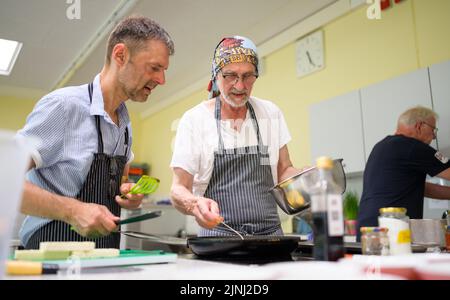 PRODUCTION - 30 June 2022, Lower Saxony, Lüneburg: Winfried Marx, professional chef (r), gives Sven (l) tips on frying at the cooking group for grieving widowers. The members of the small group, which meets once a month in Lüneburg to cook, are between 59 and 87 years old. A professional guides the widowers. (to dpa-KORR 'Cooking group for grieving widowers - ready-made meals are taboo') Photo: Philipp Schulze/dpa Stock Photo
