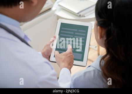 Over shoulder view of male and female physicians gathered together at modern office and using digital tablet while discussing possible treatment for patient Stock Photo