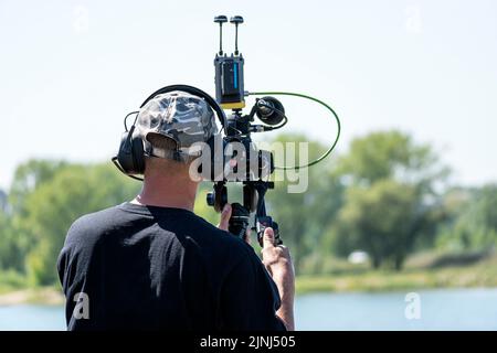Black camera with a microphone in hand on a blurry light green background. The video operator makes a video recording of the film. Stock Photo