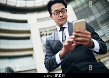 Low angle view of Asian businessman text messaging on smartphone in airport Stock Photo