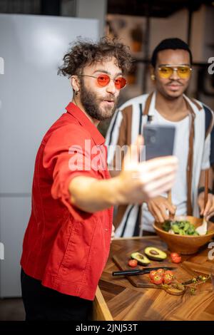 Two brightly dressed stylish guys taking selfie on phone indoors Stock Photo