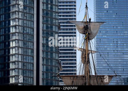 The crew of the replica sailing ship, Gotheborg, perform repairs and maintenance up the tall rigging while docked beneath the high-rise towers at South Quay, Canary Wharf in London Docklands, during its four-day visit to the capital before it continues its two-year around the world expedition to Shanghai, China, on 9th August 2022, in London, England. Londoners are invited to tour the decks of this facsimile of the original ship which sank off the Swedish coast in 1745. Its main cargo would have been tea, porcelain, herbs and silk on the China route.