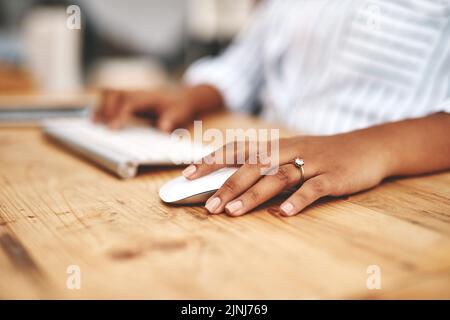 Hand on a mouse, clicking and scrolling while browsing online and surfing the internet. Closeup of a woman using a computer while sitting at a wooden Stock Photo