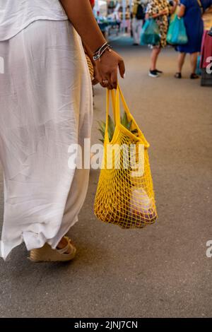 Woman in white dress with shopping in reusable cotton net bag at local market, zero waste concept. Stock Photo