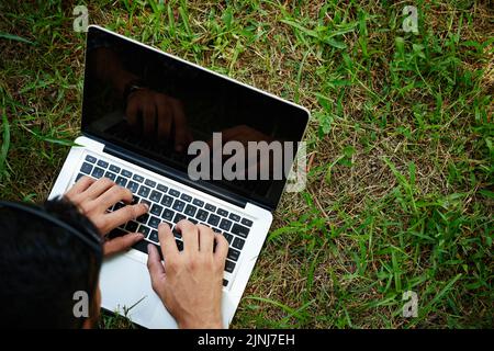 Close-up shot of unrecognizable man lying on green lawn and using modern laptop while spending weekend outdoors Stock Photo