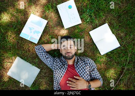Handsome bearded manager lying on green lawn with closed eyes while taking break from work, documents and notepad illuminated with sunbeams Stock Photo
