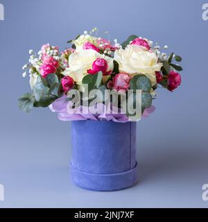Delicate holiday bouquet in a blue velor round gift box on a blue background. Bouquet with beige and pink roses, white gypsophila and eucalyptus twigs Stock Photo