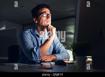Businessman thinking of ideas in front of a computer while working late in an office at night. Hard Working entrepreneur sending emails, online Stock Photo