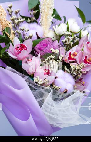 Close up of floral bouquet of fresh natural ingredients wrapped in floral tracing paper. Festively packaged bouquet in pink style composed of irises, Stock Photo