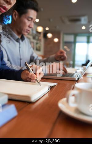 Group of hard-working white collar workers wrapped up in work while sitting at wooden table of cozy small coffeehouse, close-up shot Stock Photo
