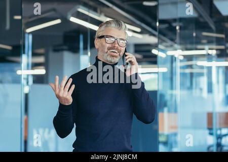 Senior gray haired businessman owner talking on phone in modern office, successful investor smiling in glasses Stock Photo