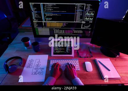 Concentrated male software developer wrapped up in work while sitting in front of computer at dim office, close-up shot Stock Photo
