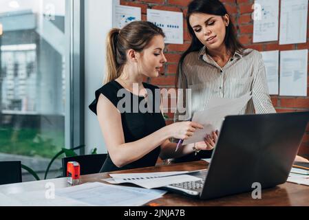 Female secretary looking concerned while her boss checking document sitting at desk in modern office. Stock Photo