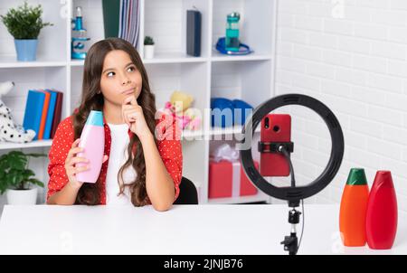 Child vlogger making video blog on phone. Blogging weblog and vlog. Teen girl blogger influencer hold hair conditioner or shampoo bottle recording Stock Photo