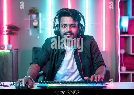 Excited gamer with headphones playing online video game by looking camera at home on neon background - concept of social media live stramer Stock Photo