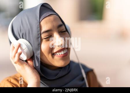 Muslim woman enjoying while listening to music outdoors Stock Photo