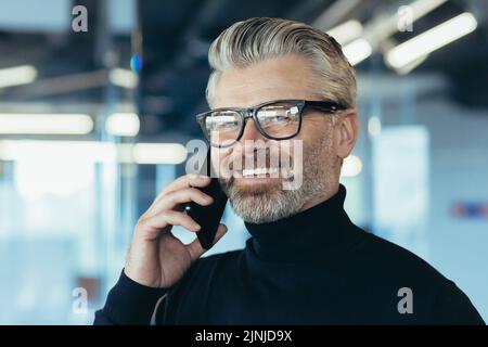 Close-up photo portrait of senior experienced male salesman, businessman in glasses and beard smiling and looking at camera, successful banker investor working in modern office, boss at work Stock Photo