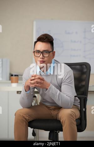 Attractive young Vietnamese business executive sitting in armchair in his office Stock Photo
