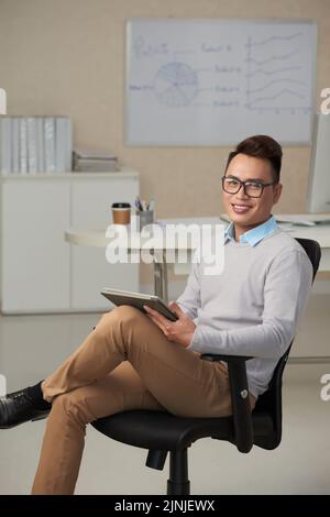 Portrait of young Vietnmaese entrepreneur with tablet computer working in his office Stock Photo