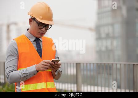 Construction site worker reading messages on his smartphone Stock Photo