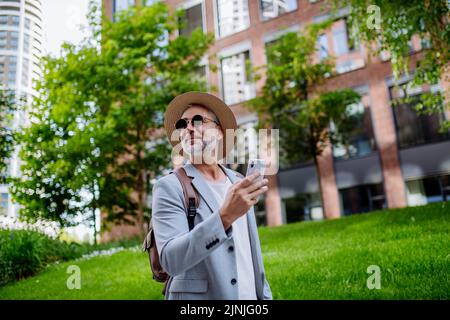 Confident man wearing straw hat and backpack,using phone, businessman in casual clothes in summer on the way to work. Stock Photo