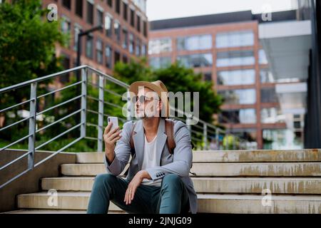 Confident man wearing straw hat and backpack,using phone, businessman in casual clothes in summer on the way to work. Stock Photo