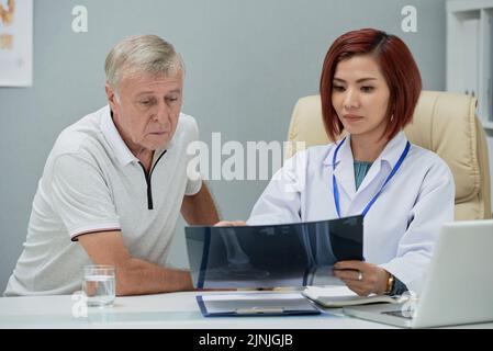 Vietnamese female doctor showing feet x-ray to senior patient Stock Photo