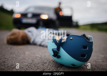 Little boy fallen from bicycle and lying still on road after car accident. Stock Photo