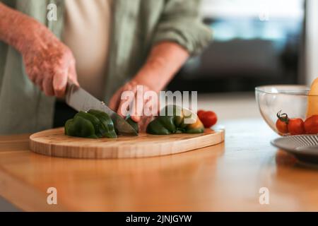 Close-up of senior man preparing vegetable, cutting at wooden board, healthy lifestyle concept. Stock Photo