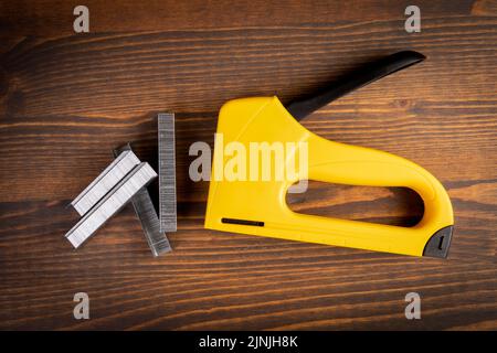 Yellow plastic staple gun and metal staples on wooden background. Stock Photo