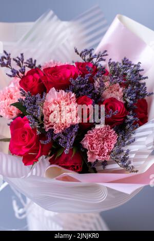 Close up of a bouquet of red and pink flowers wrapped in festive paper on a blue background. Festively packed bouquet in red and purple colors. Concep Stock Photo