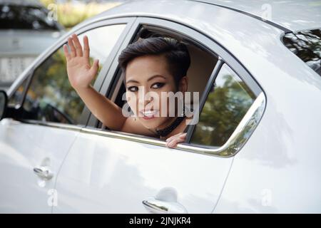 Beautiful woman sitting on back seat of car an waving to pedestrians Stock Photo