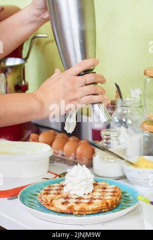 Hands of woman putting whipped cream on fresh waffles Stock Photo
