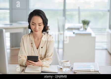 Chinese entrepreneur using calculator to check figures in business report Stock Photo