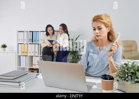 Female entrepreneur with telephone receiver checking data on laptop screen Stock Photo