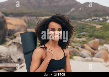 Portrait of a young smiling woman holding a mat against beautiful landscape Stock Photo