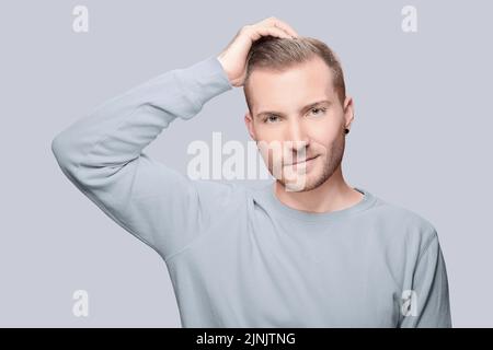 A serious shy guy with a hand high on his head look straight into camera Stock Photo