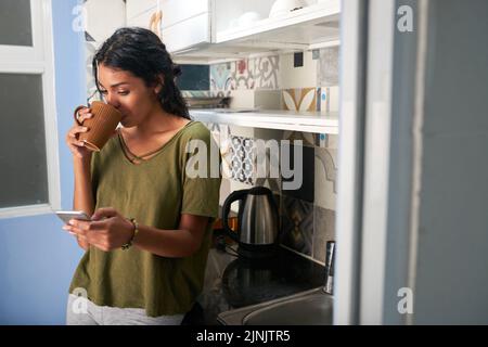 Pretty Hispanic woman drinking morning coffee and checking messages in her smartphone Stock Photo